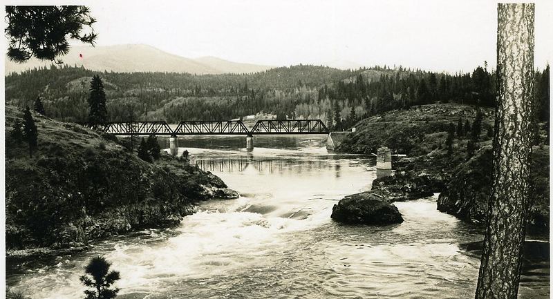 Vintage sepia postcard of Albeni Falls, with whitewater below a steel railroad bridge